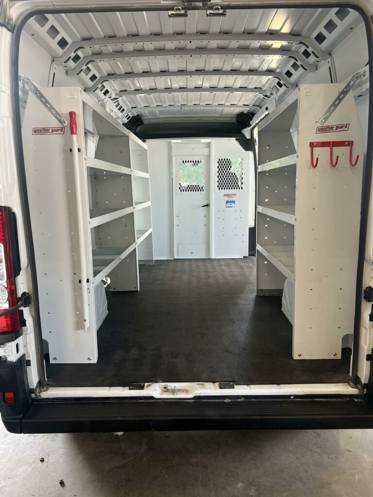 Interior of a work van that has shelving lining both sides along with a partition before the driver's compartment