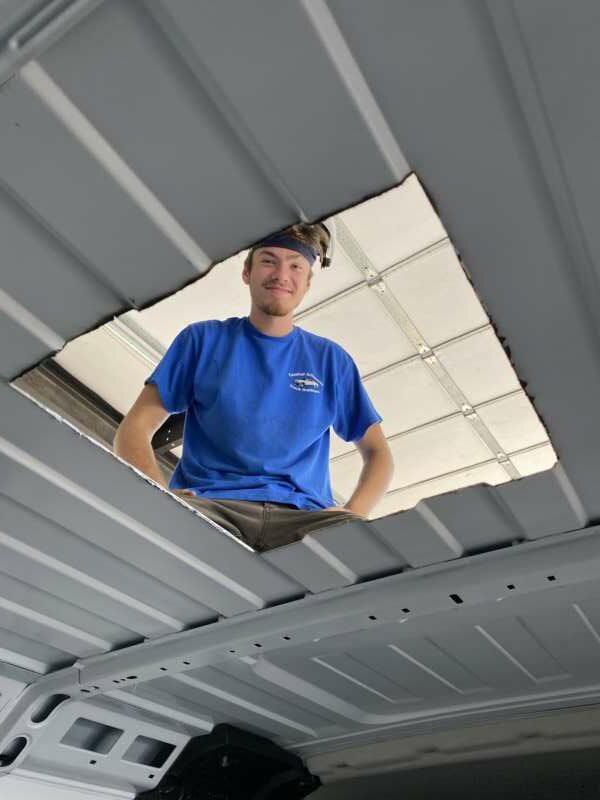 young man looks through cut out square in roof of van